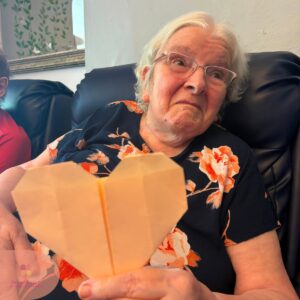 Resident proudly holding a handmade paper heart during a creative craft session.