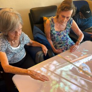 Two elderly residents exploring interactive nature scenes on a touch table during a care home activity.