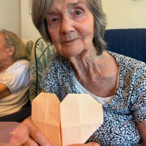 Resident smiling while proudly displaying a completed paper heart craft.