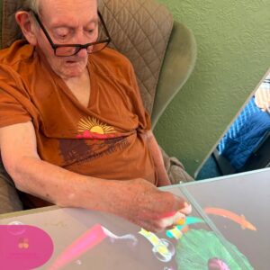 Elderly resident engaging with colourful interactive touch table activities in a comfortable care home lounge.