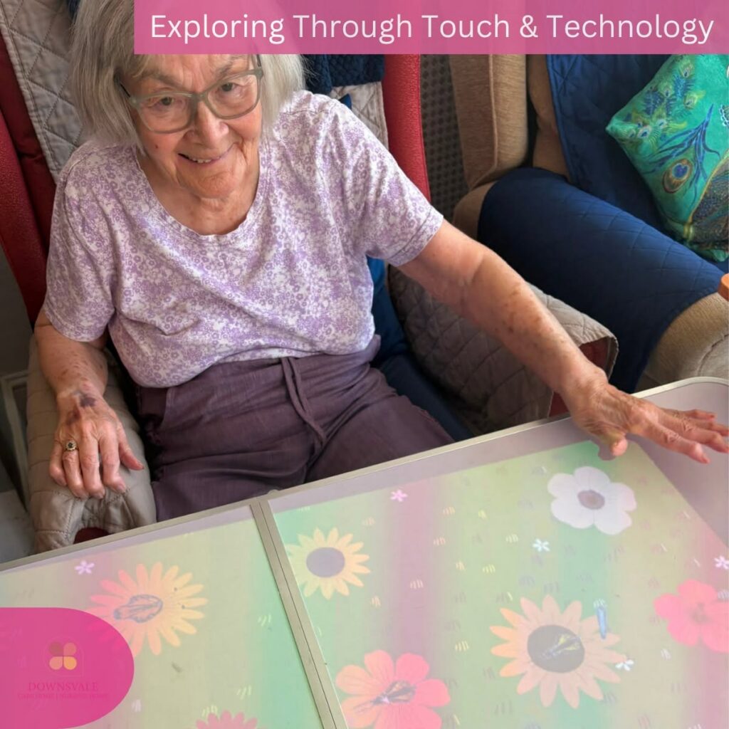 Smiling elderly resident using an interactive touch table with colourful flower-themed sensory activities.