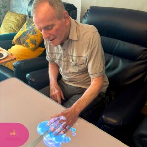 Elderly resident enjoying a sensory touch table activity with colourful bubbles in a care home.
