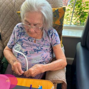 Elderly resident creating colourful pipe cleaner art during a care home activity.