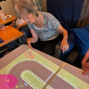 Elderly resident playing an interactive touch table racing game during a care home activity session.