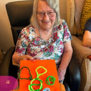 Happy care home resident displaying a colourful handmade craft creation.