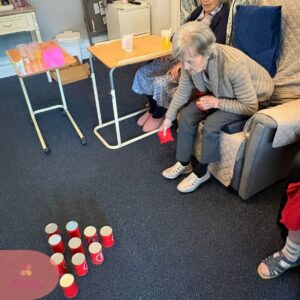 An elderly resident plays a bean bag tossing game to improve coordination and enjoy a friendly activity.