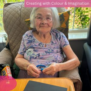 Smiling elderly resident enjoying a creative pipe cleaner activity in the care home.