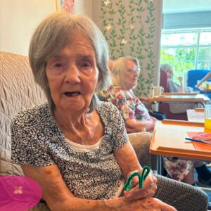 Care home resident proudly holding a handmade pipe cleaner craft.