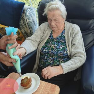 An elderly resident decorates a cupcake with icing during a creative baking activity.
