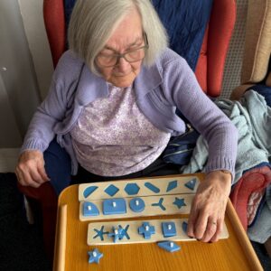 A resident concentrates on completing a wooden shape puzzle to support cognitive skills.
