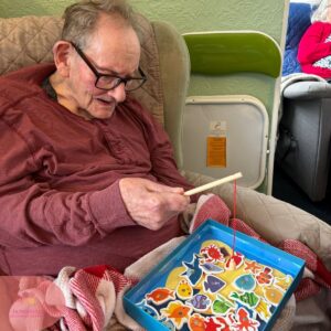 A resident smiles while playing a magnetic fishing game as part of a stimulating care home activity.