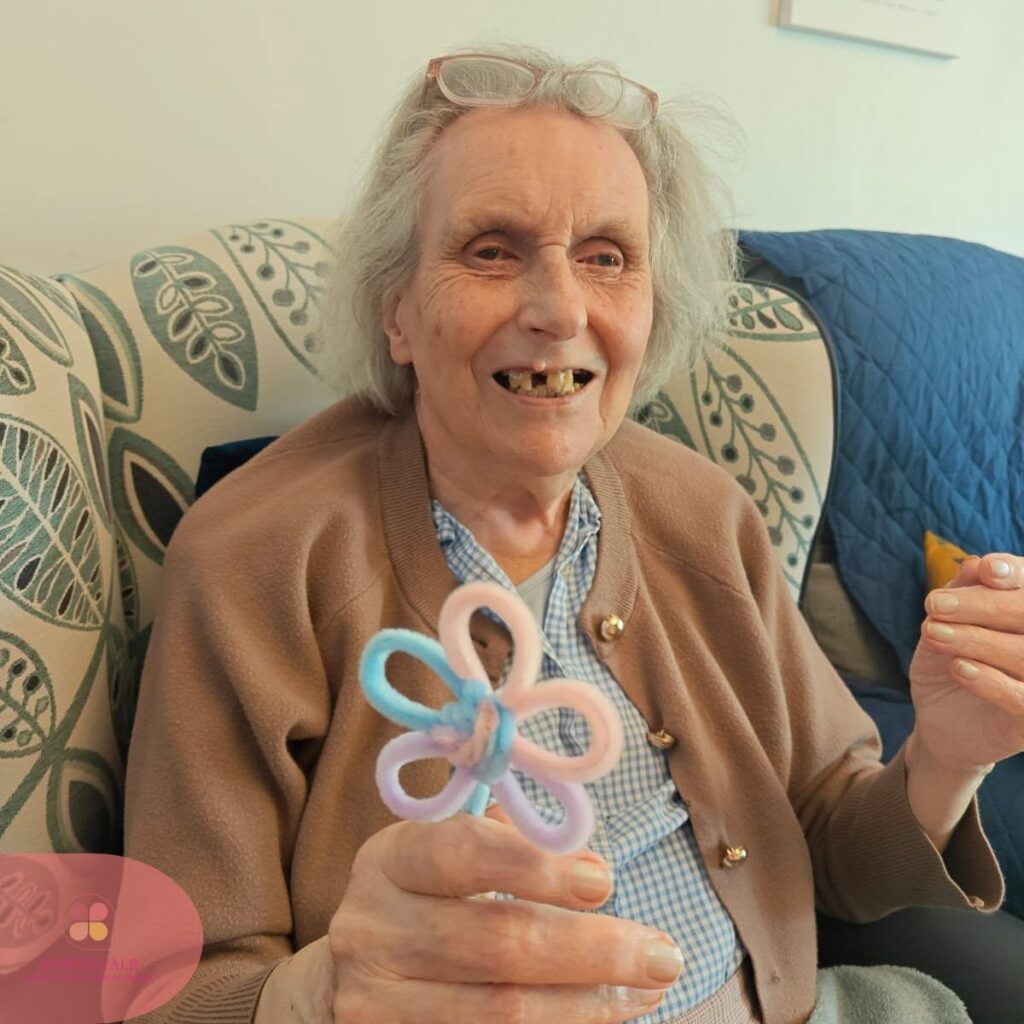 A smiling resident proudly holds a handmade pipe cleaner flower after a creative craft activity.