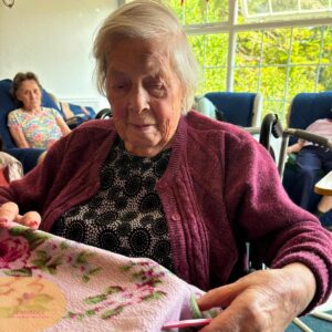Smiling elderly resident exploring a soft floral blanket during a sensory session.