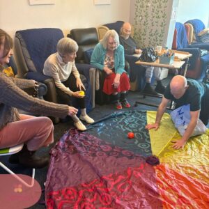 Residents enjoy an interactive group game using a colorful parachute during a fun care home activity.