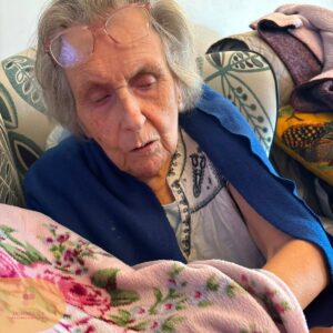 Elderly resident wrapped in a blue blanket touching a soft floral blanket.