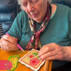 Resident carefully placing colourful diamond beads onto a flower craft with a precision tool.