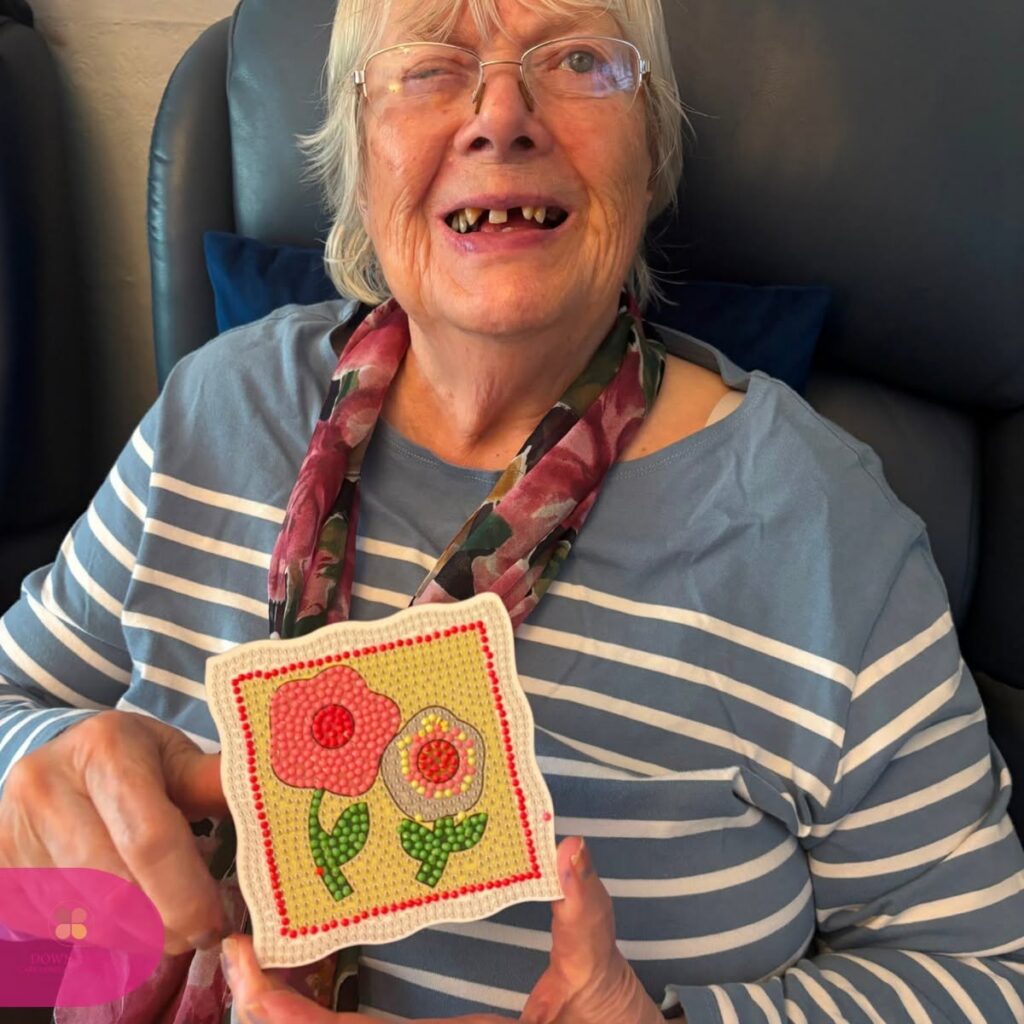 Resident smiling proudly while holding a colourful diamond art flower design they completed.