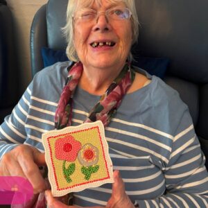 Resident smiling proudly while holding a colourful diamond art flower design they completed.