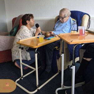 Performer singing with a resident, creating a warm and interactive musical experience.