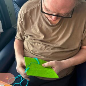 Resident carefully completing a woollen yarn craft activity with bright blue thread.