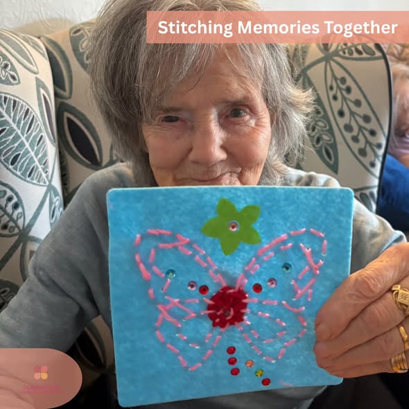 Resident proudly holding a completed butterfly stitching craft with a smile.