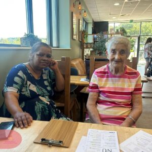 Care home resident and carer relaxing together at a café.