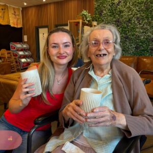 Resident and companion holding hot drinks during a café visit.