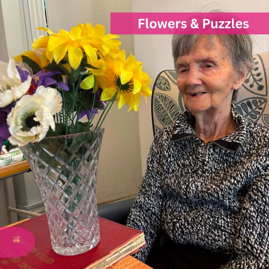 Smiling elderly woman beside a vase of flowers.