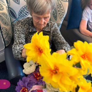 Elderly woman enjoying a flower arranging activity.