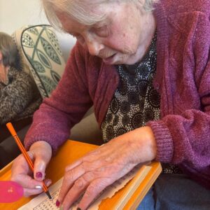 Elderly woman writing at a table during an activity.