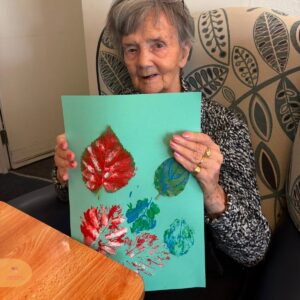 Elderly woman holding a colourful leaf-print artwork.