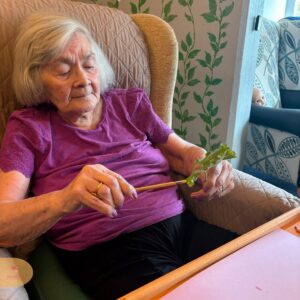 Elderly woman painting a leaf with a brush.