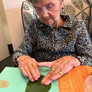 Elderly woman pressing a leaf onto paper.