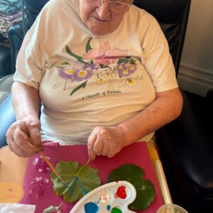 Resident painting leaves on coloured paper.