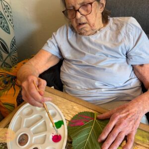 Elderly woman painting leaves with a brush.