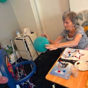 An elderly woman reaches out to catch a blue ball during an activity.