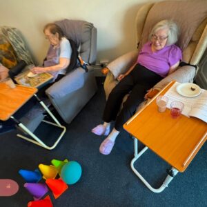 Two elderly women sit in armchairs during a group activity.
