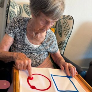 Elderly woman concentrating while pointing to colored shapes on an activity board.