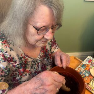 Elderly woman preparing soil in a plant pot.