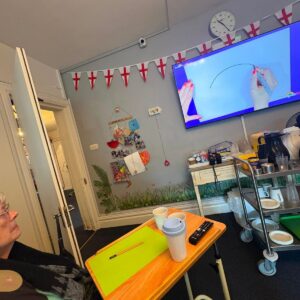 Elderly woman watching a drawing activity on a television.
