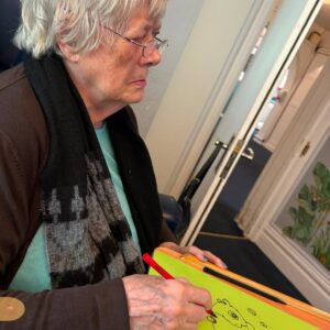 Elderly woman drawing on a green board with colored markers.