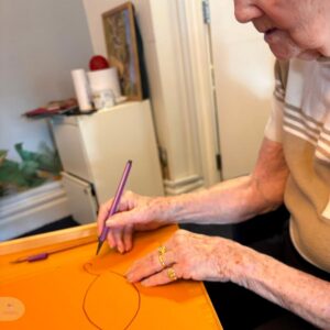 Older woman drawing a simple shape on a table.