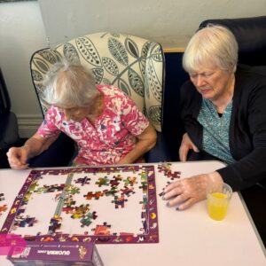 Elderly women assembling a colorful jigsaw puzzle at a table.