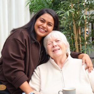 A care home staff member smiling and putting her arm around an elderly resident.