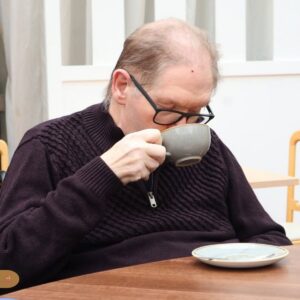 An elderly man enjoying a cup of coffee in a care home lounge.