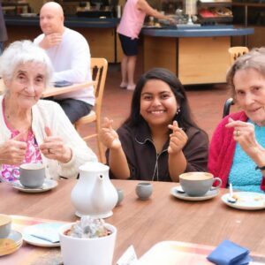 An elderly woman, a young woman, and another older woman enjoying coffee together at a café, sharing smiles and a cheerful moment.