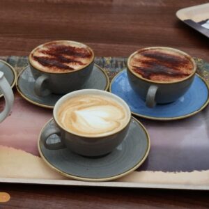 Three cups of coffee with latte art and chocolate powder, served on ceramic saucers on a wooden café table.