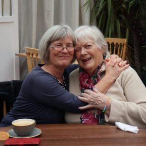 Two older women sharing a warm hug and smiling together at a care home.